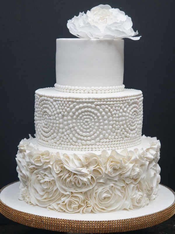 A white wedding cake with pearls and ruffles on it