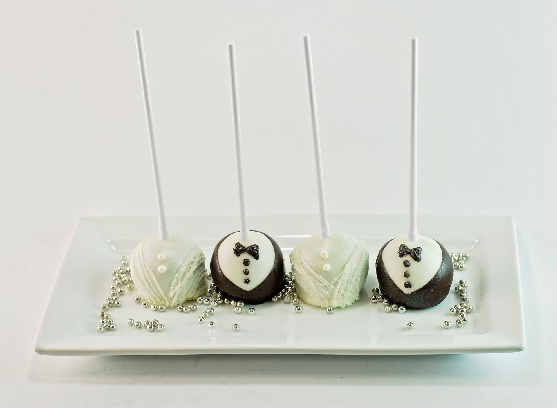 A white plate topped with four cake pops in tuxedos