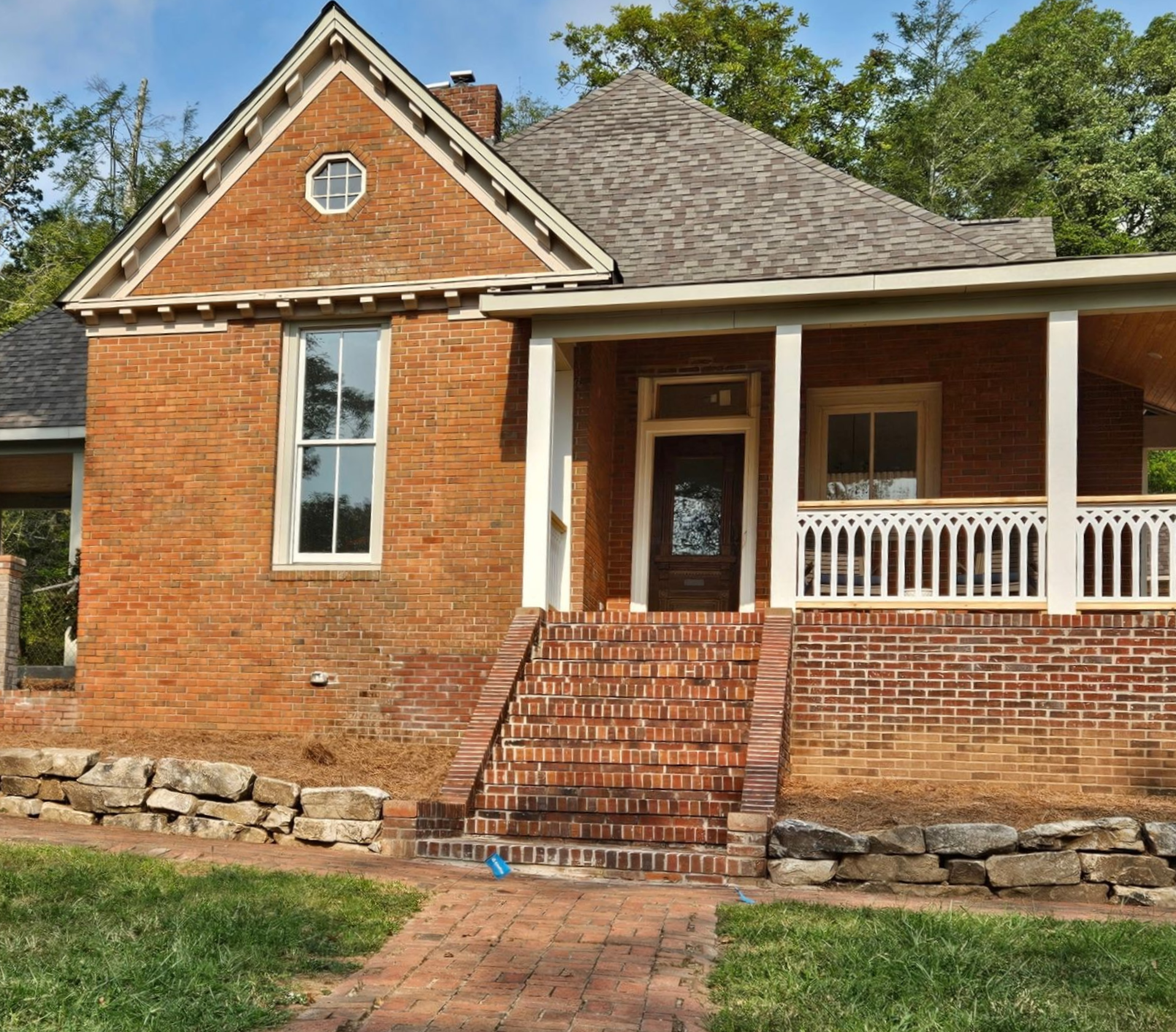A brick house with a porch and a driveway in front of it.