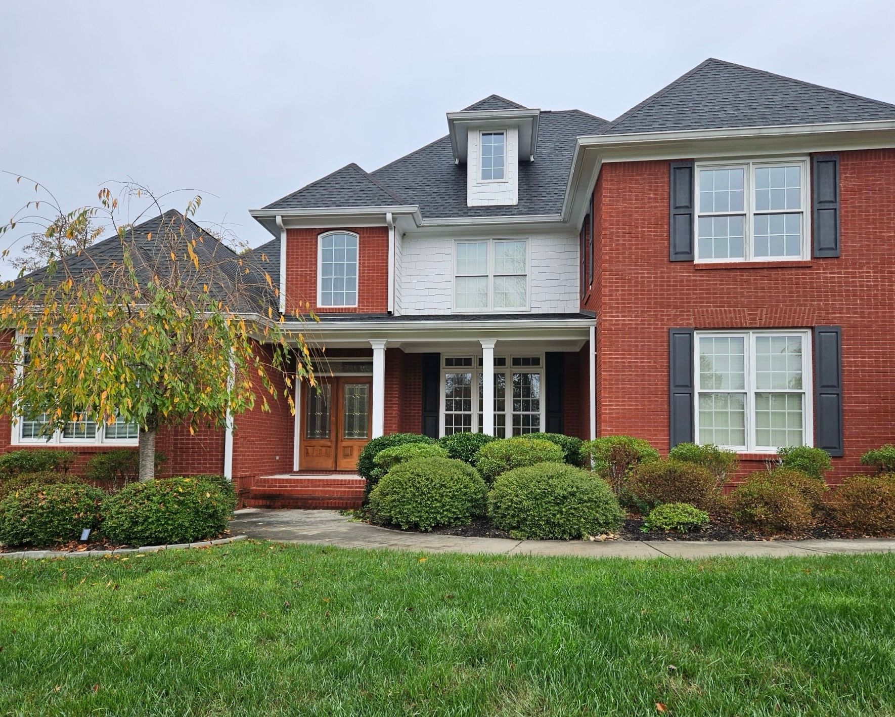 A large red brick house with black shutters and a large lawn in front of it.