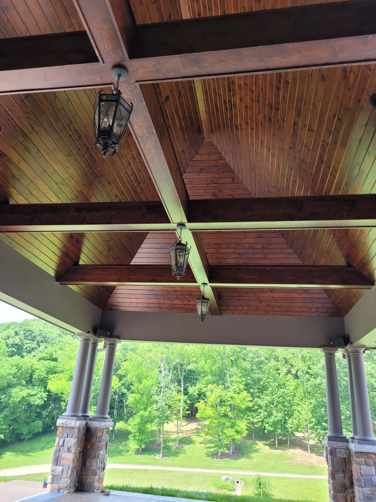 The ceiling of a porch with wooden beams and lanterns hanging from it.