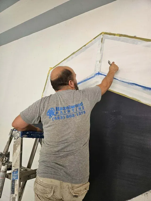 A man is standing on a ladder painting a wall.