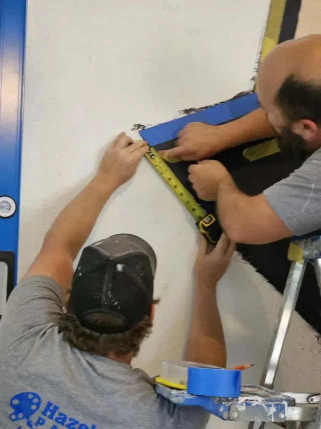 Two men are measuring a wall with a tape measure