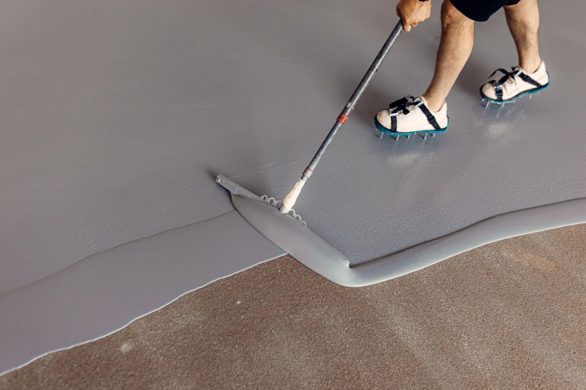 A person is painting a concrete floor with a roller.