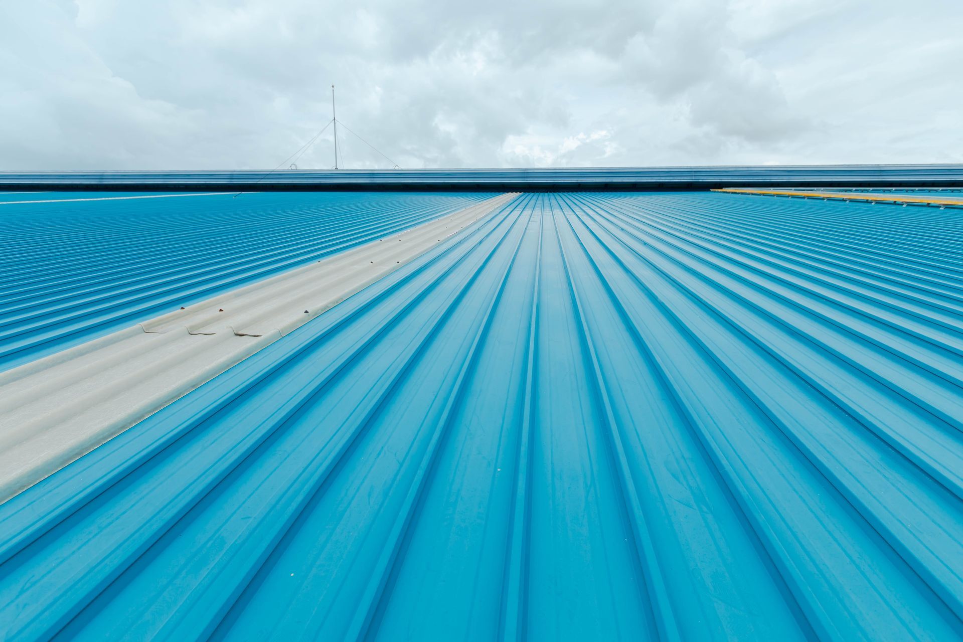 An aerial view of a blue roof with a cloudy sky in the background.