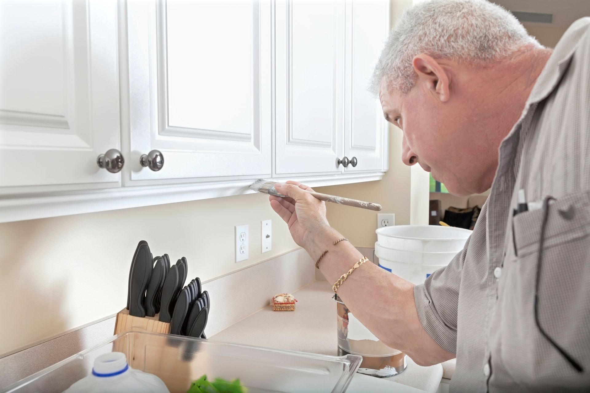 A man is painting cabinets in a kitchen with a brush.