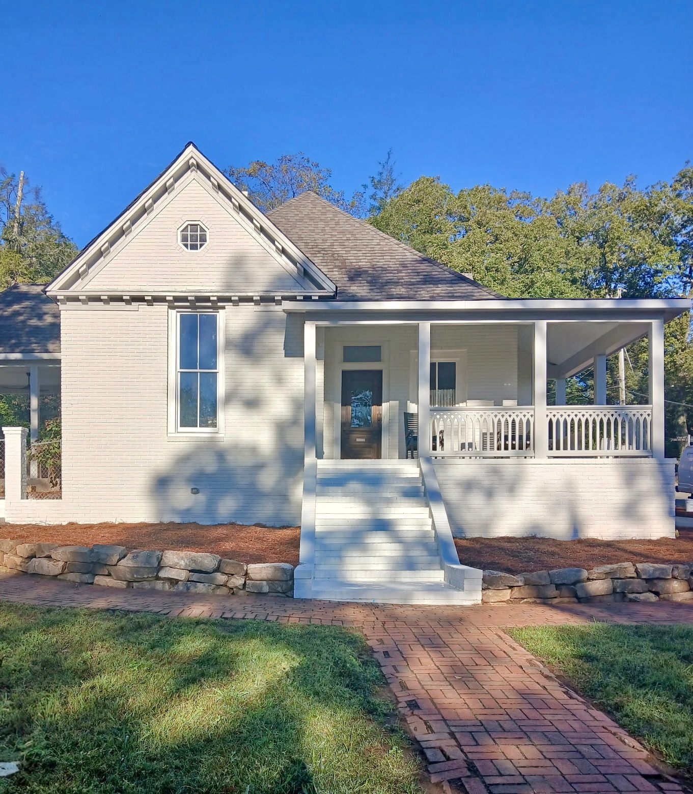 White cottage with porch, brick pathway, and stone border on a sunny day.