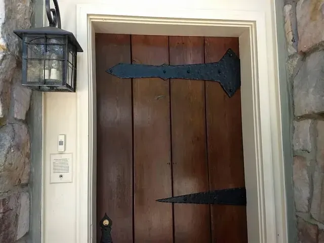 A wooden door with black hinges and a lantern on the wall.