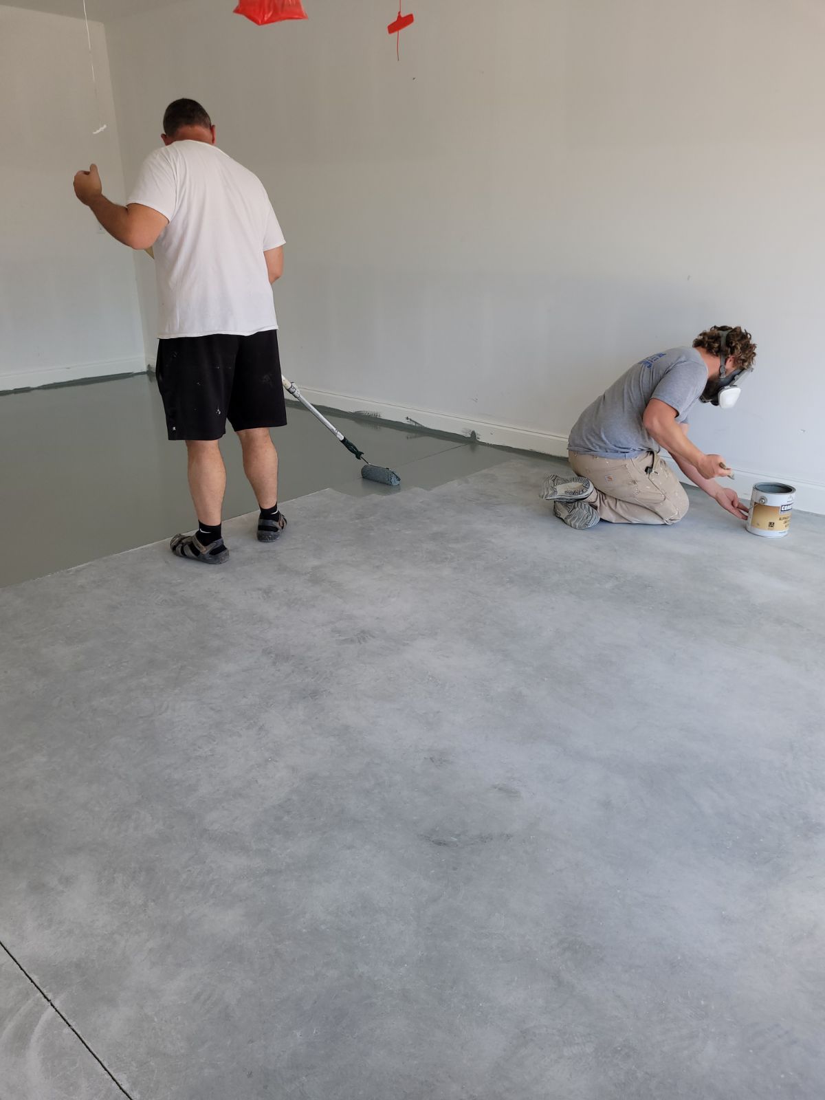 Two men are painting a concrete floor in a room