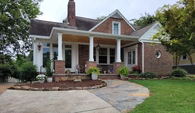 A brick house with a porch and a driveway in front of it.