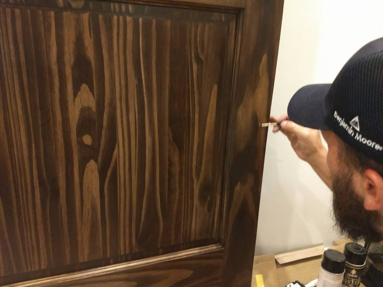 A man is painting a wooden door with a brush.