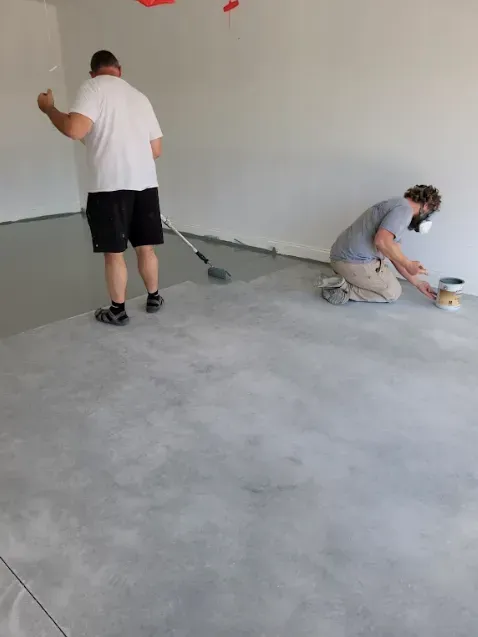 Two men are painting a concrete floor in a garage.