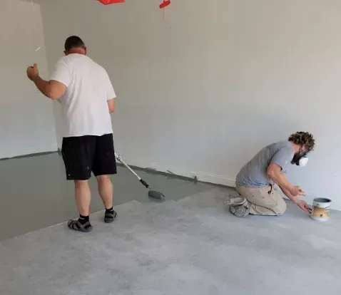 Two men are painting a wall in a room.