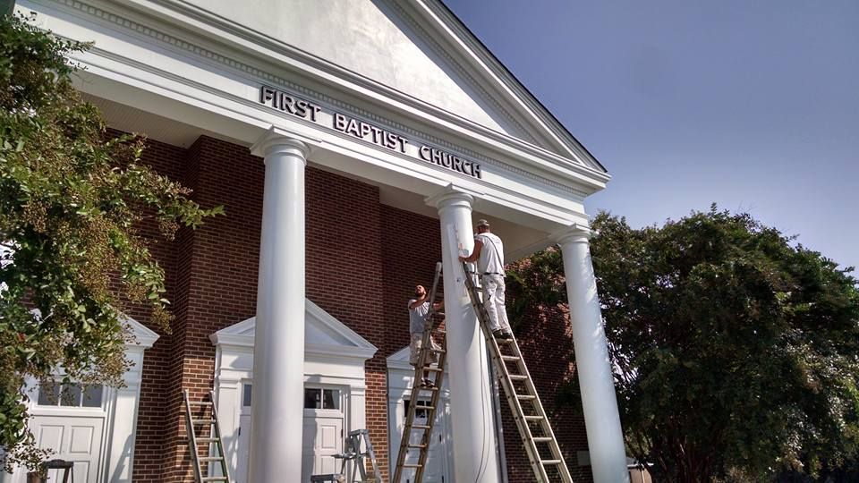 Two men are painting the front of a building that says first baptist church