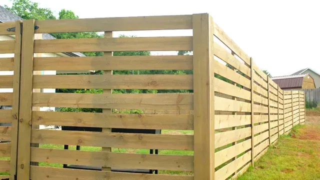 A wooden fence surrounds a grassy area with a house in the background