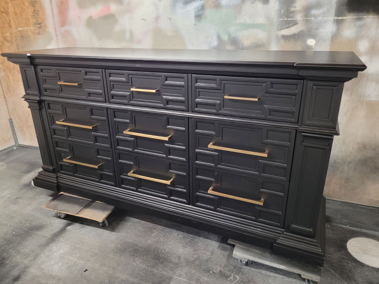 A black dresser with gold handles is sitting in a room.