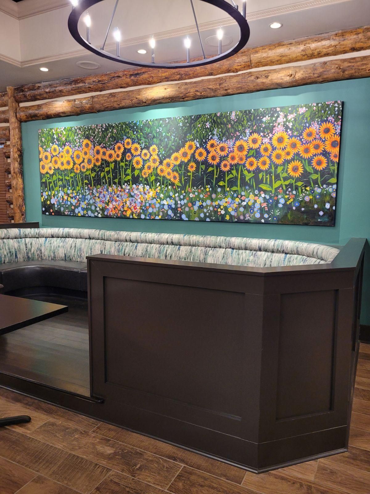 A large painting of sunflowers is hanging on a wall in a restaurant.