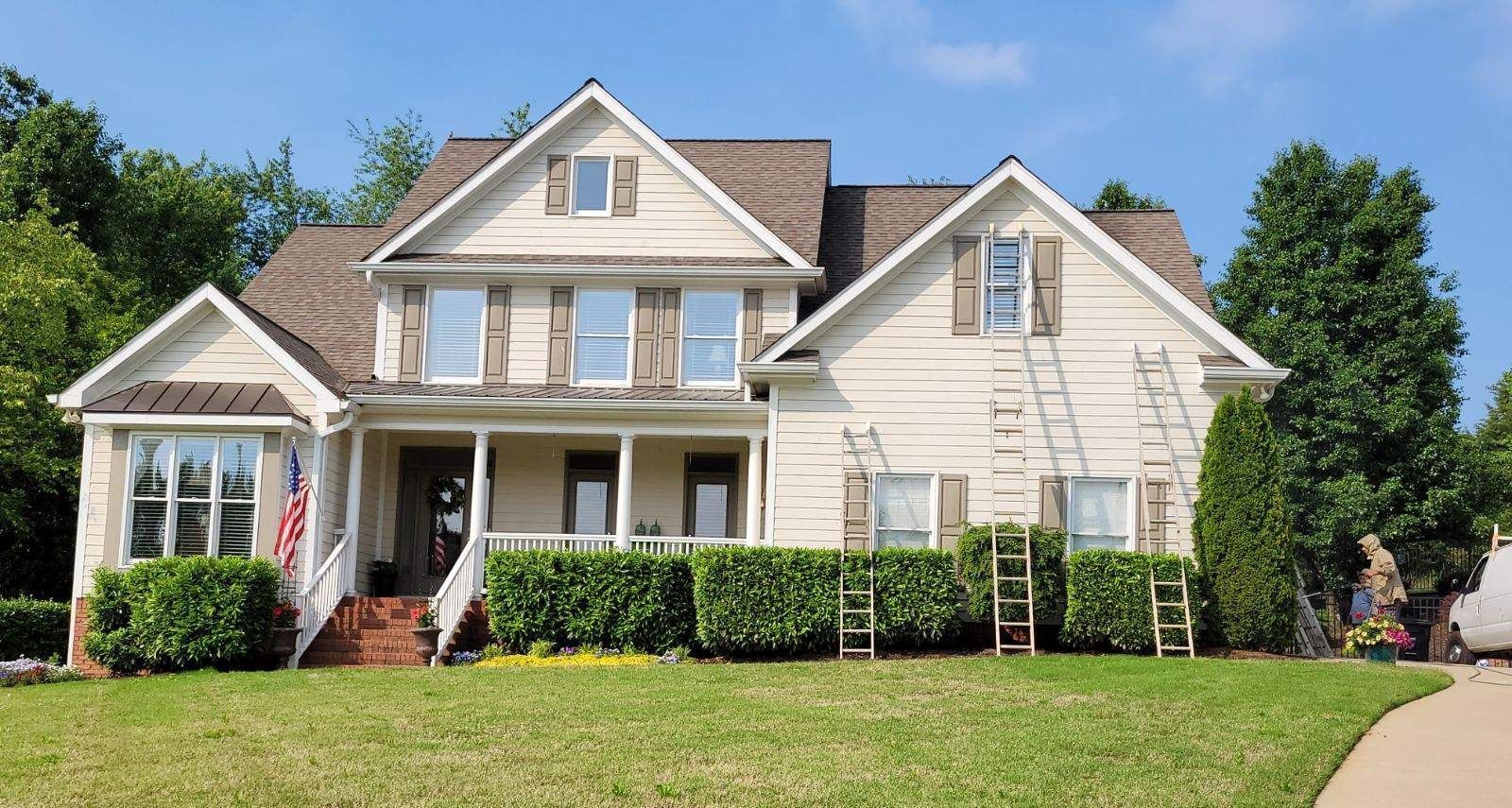 A large white house with a roof that is being painted