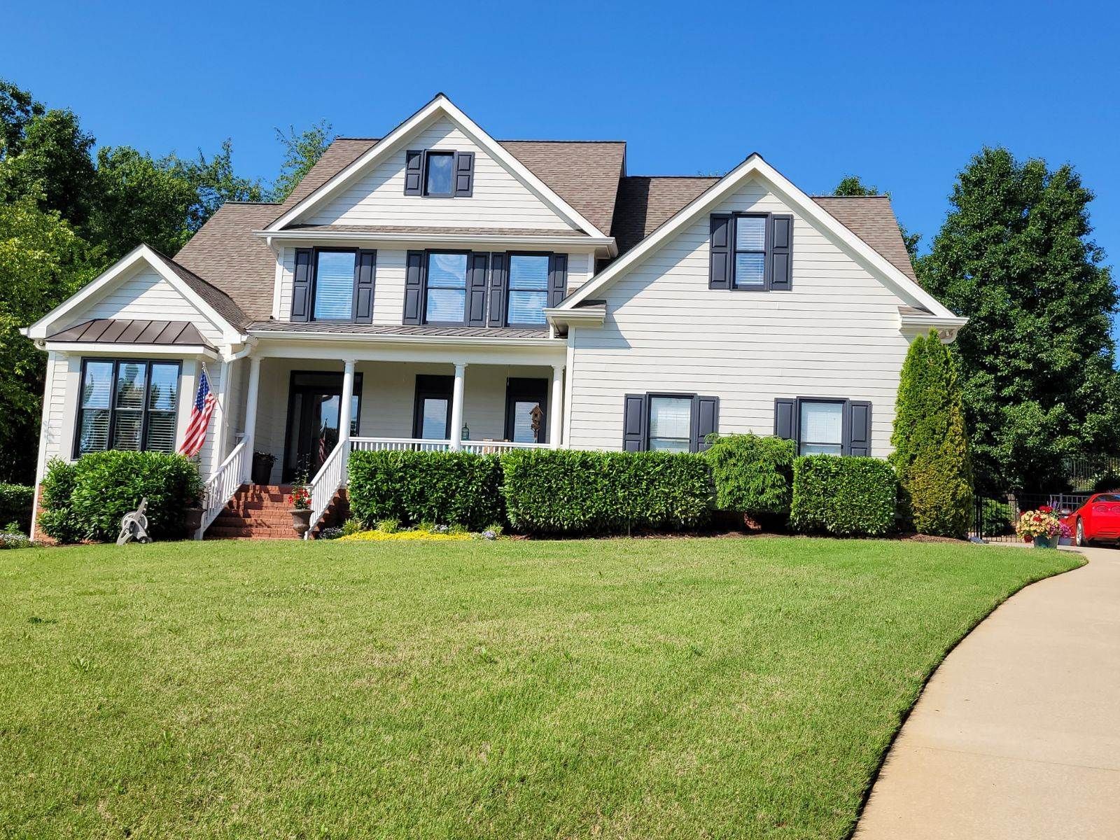 A large white house with black shutters and a red car parked in front of it.