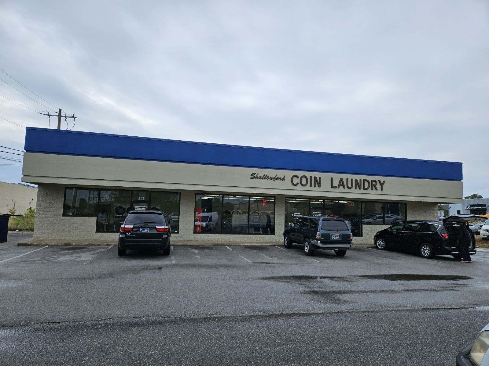 A coin laundry with cars parked in front of it.