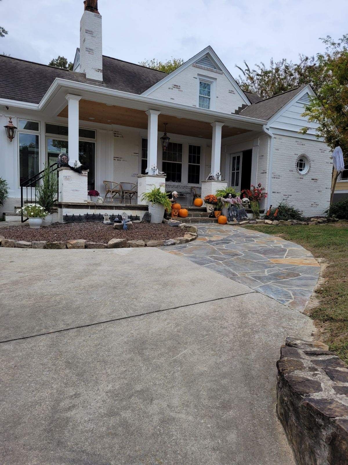 A white house with a porch and pumpkins in front of it.