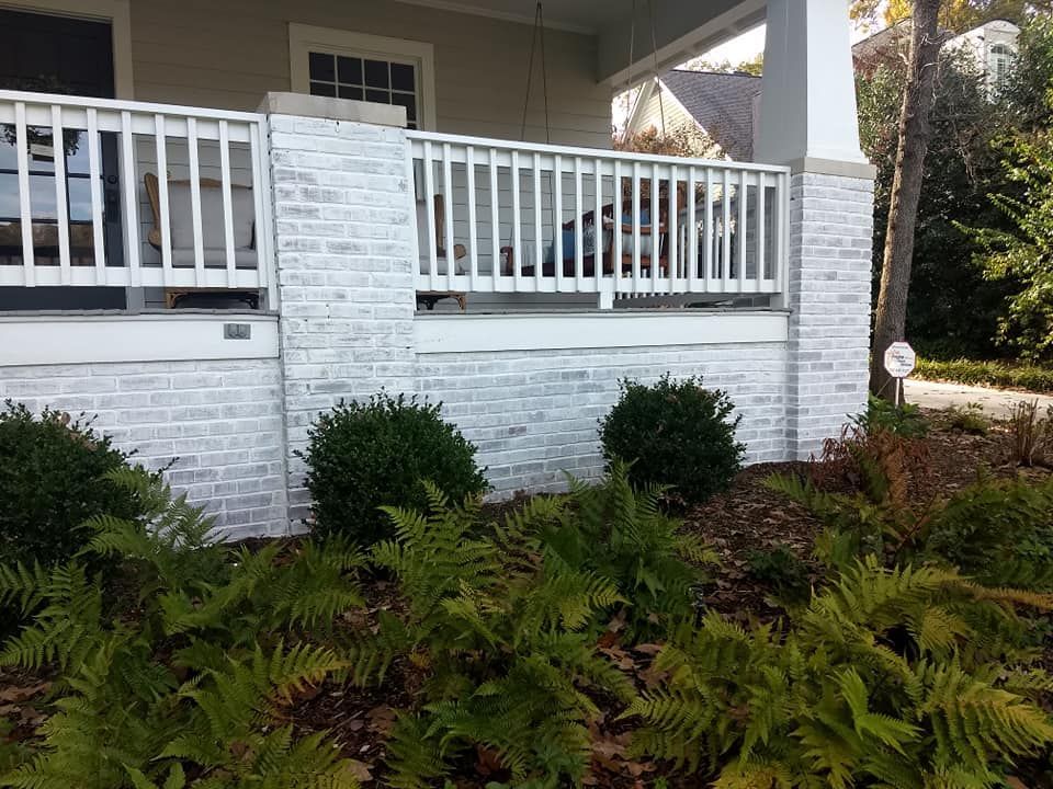 A white brick wall with a white railing and ferns in front of a house.