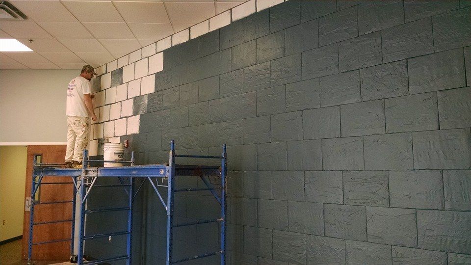 A man is standing on a scaffolding painting a brick wall.