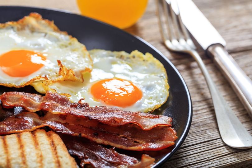 A black plate topped with eggs bacon and toast on a wooden table.