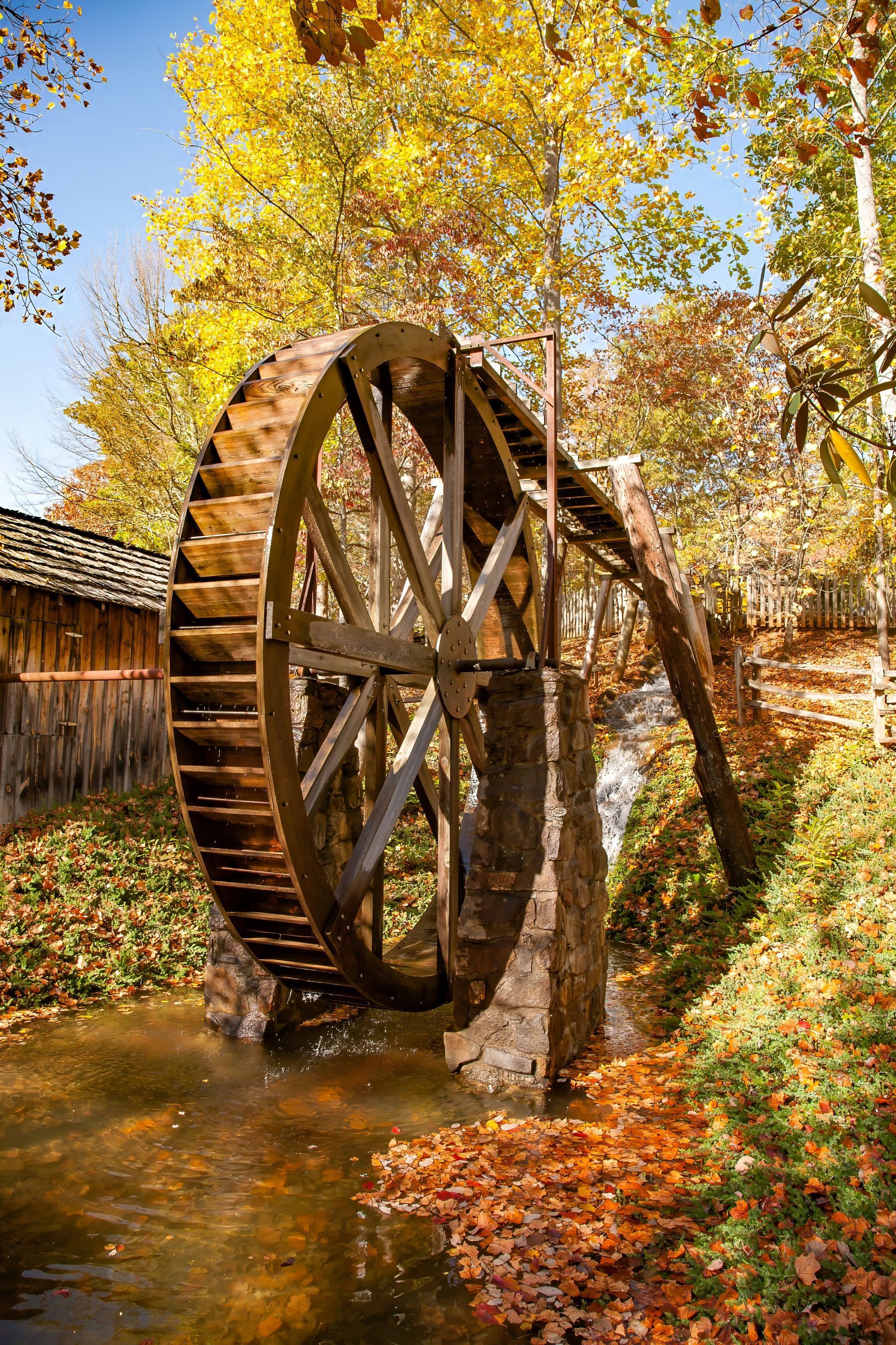 A water wheel is sitting in the middle of a river surrounded by trees.