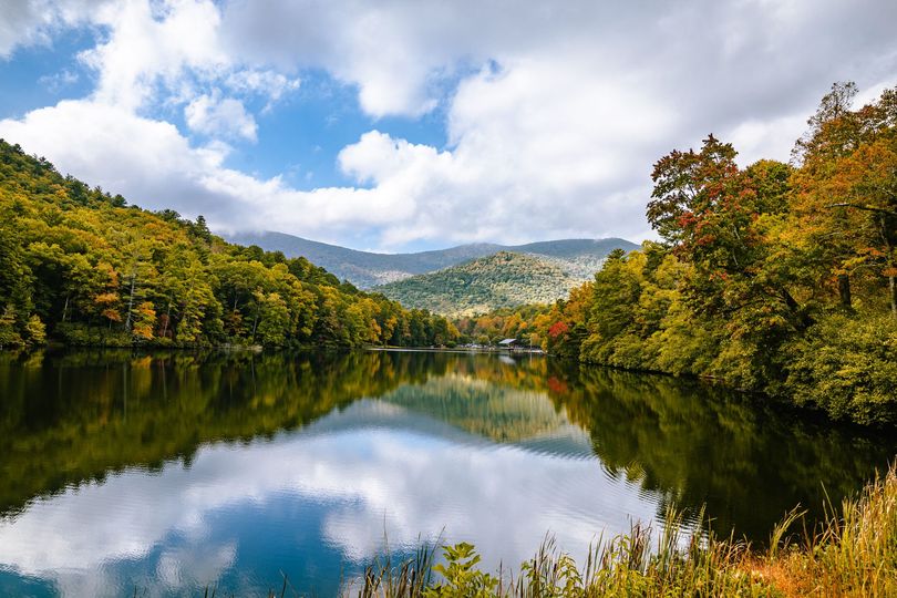 A lake surrounded by trees and mountains on a cloudy day