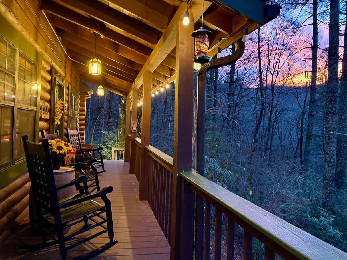 A porch with rocking chairs and a sunset in the background.