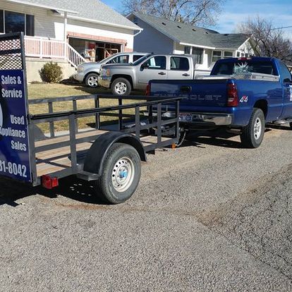 A blue truck with a trailer attached to it is parked in front of a house by payson utah appliance repair