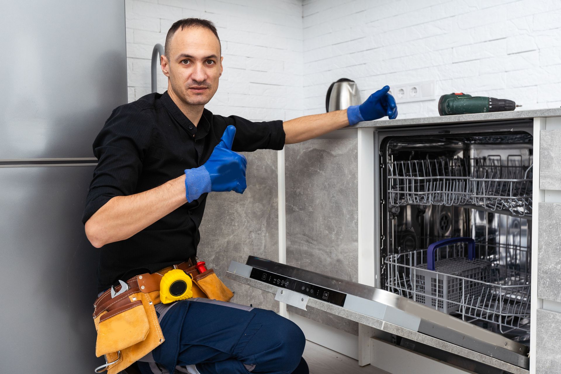 A man is fixing a dishwasher in a kitchen and giving a thumbs up.