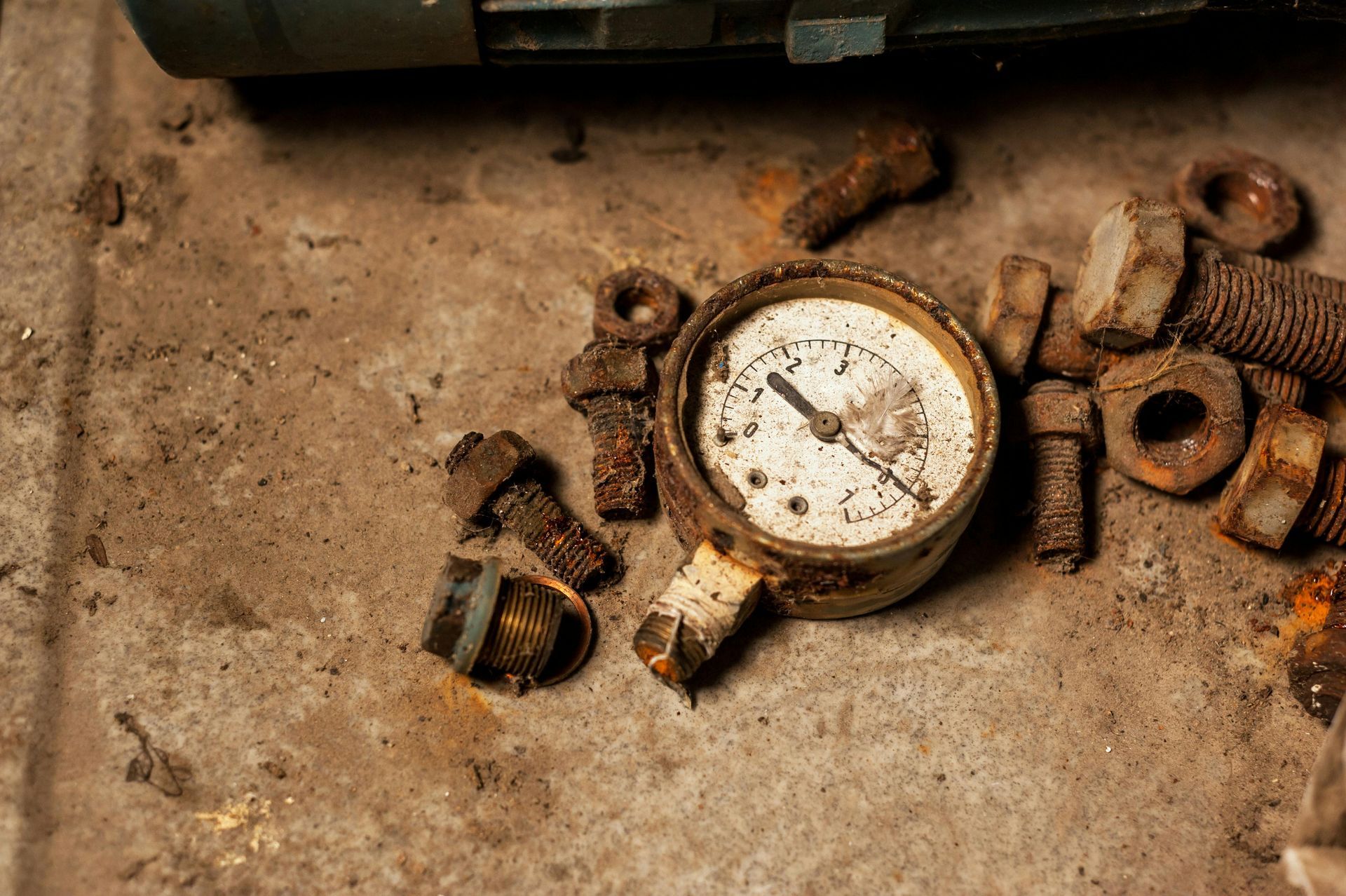 A rusty pressure gauge is sitting on top of a pile of rusty nuts and bolts.