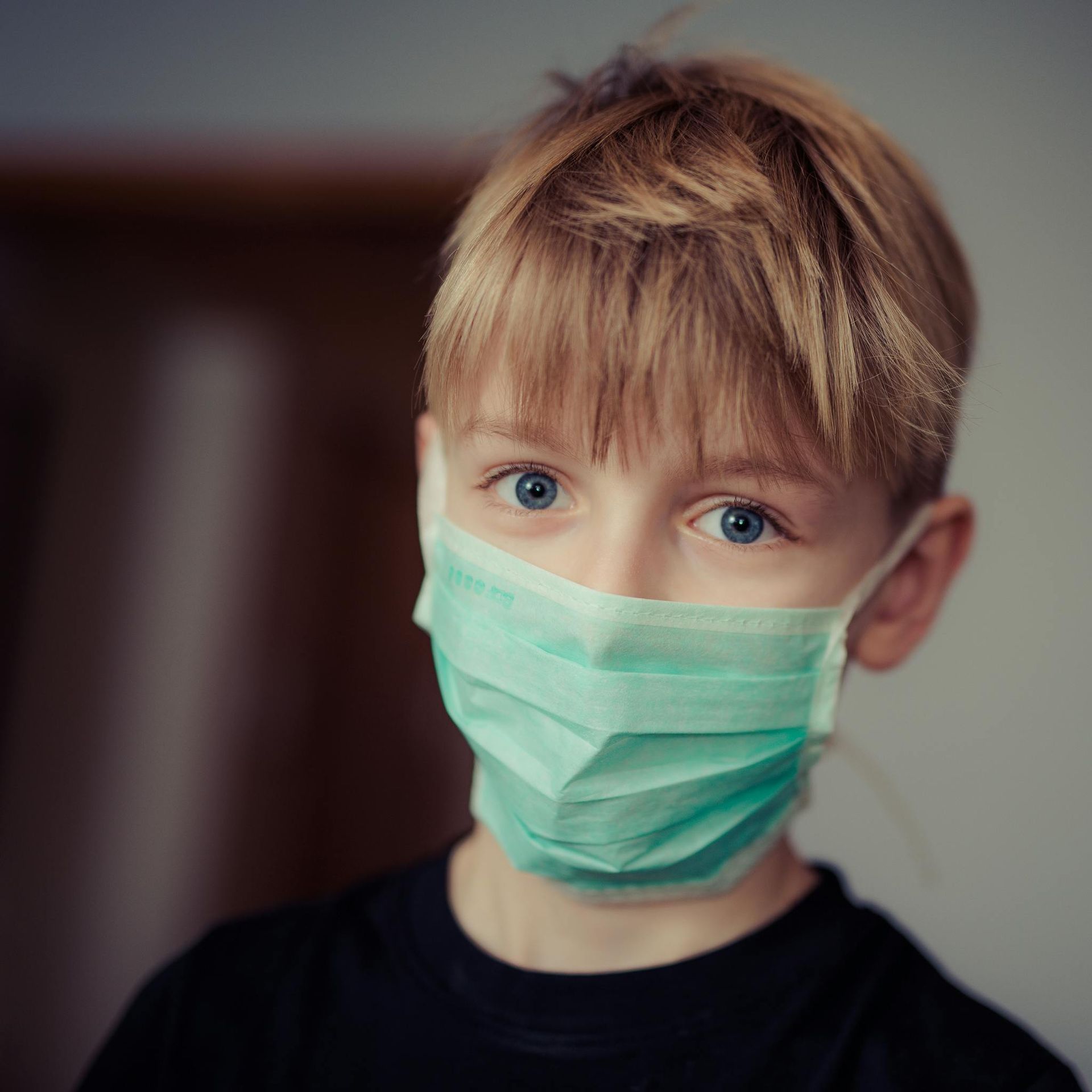 A young boy wearing a green face mask is looking at the camera.