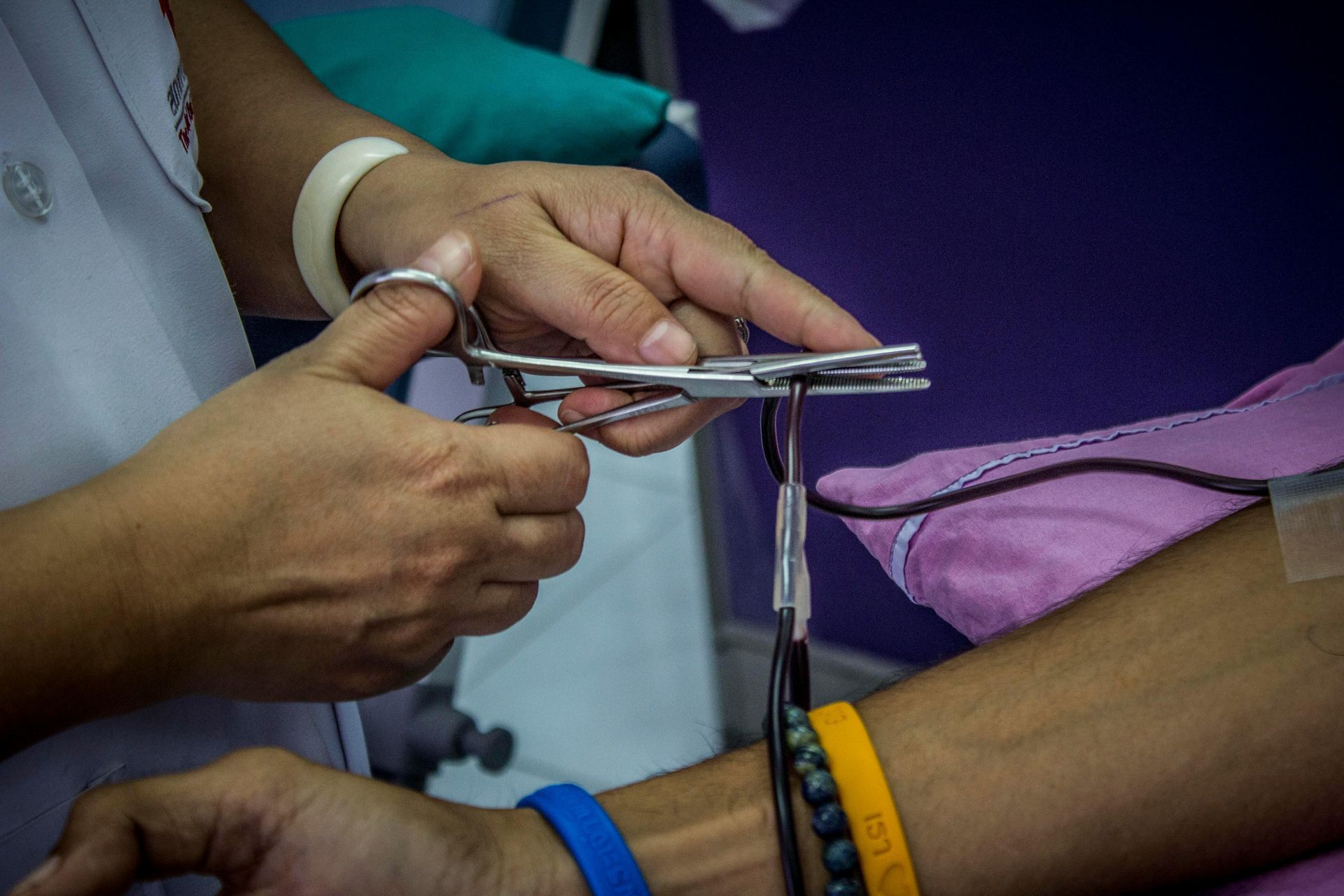 Hands cutting a purple cloth with scissors beside a person’s wrist and arm