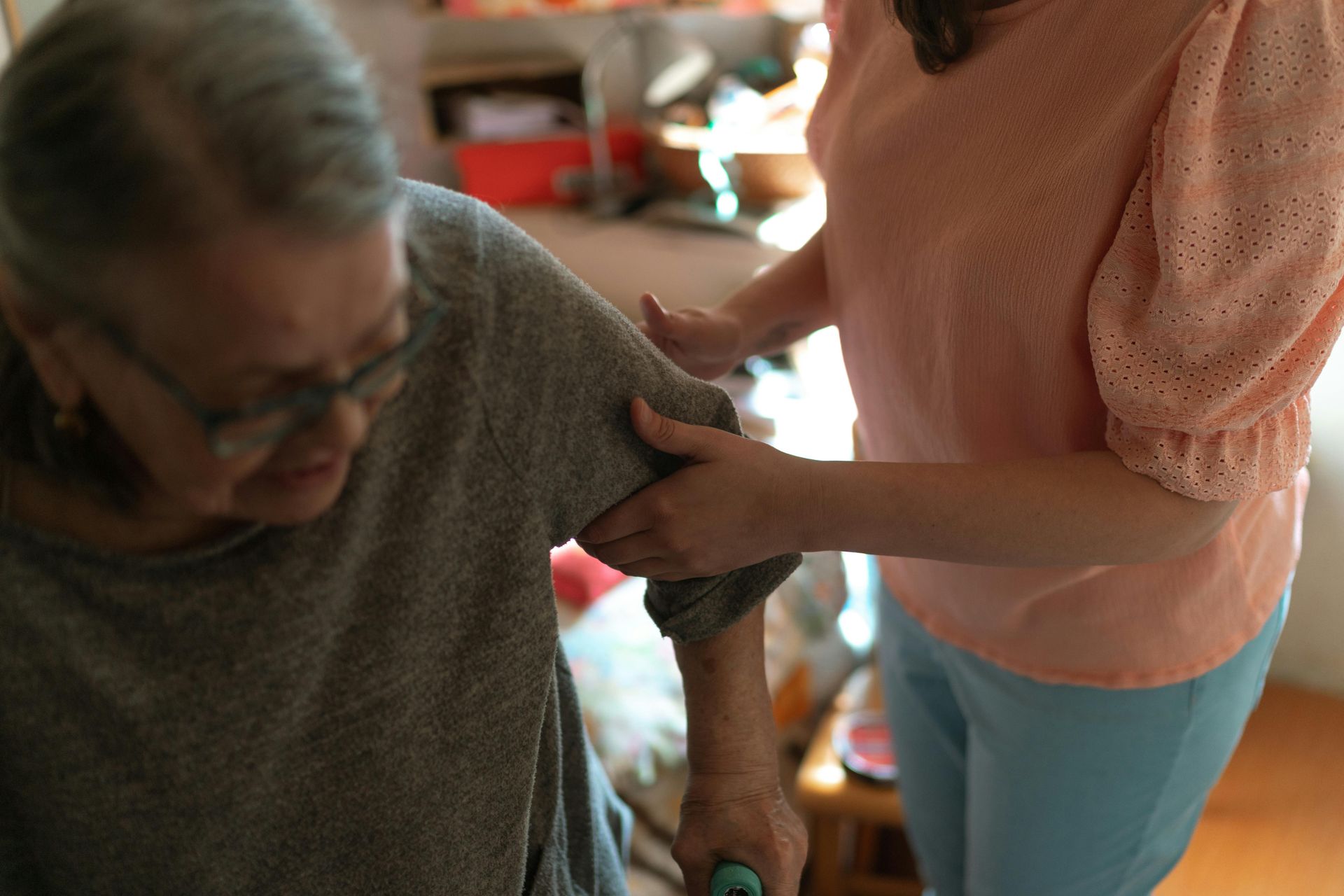 Person helping an older adult walk indoors; one holds the other's arm.
