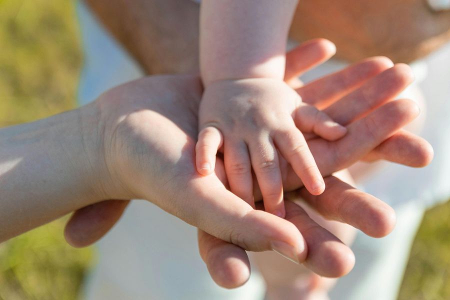 Adult and child hands clasped together outdoors in warm sunlight