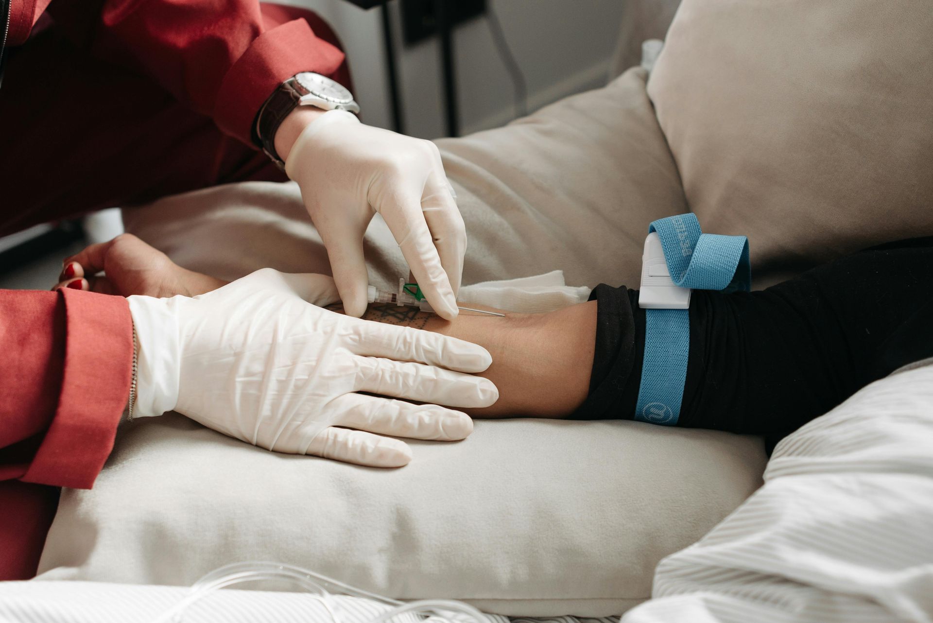 Gloved hands placing a needle in an arm during a medical procedure on a couch