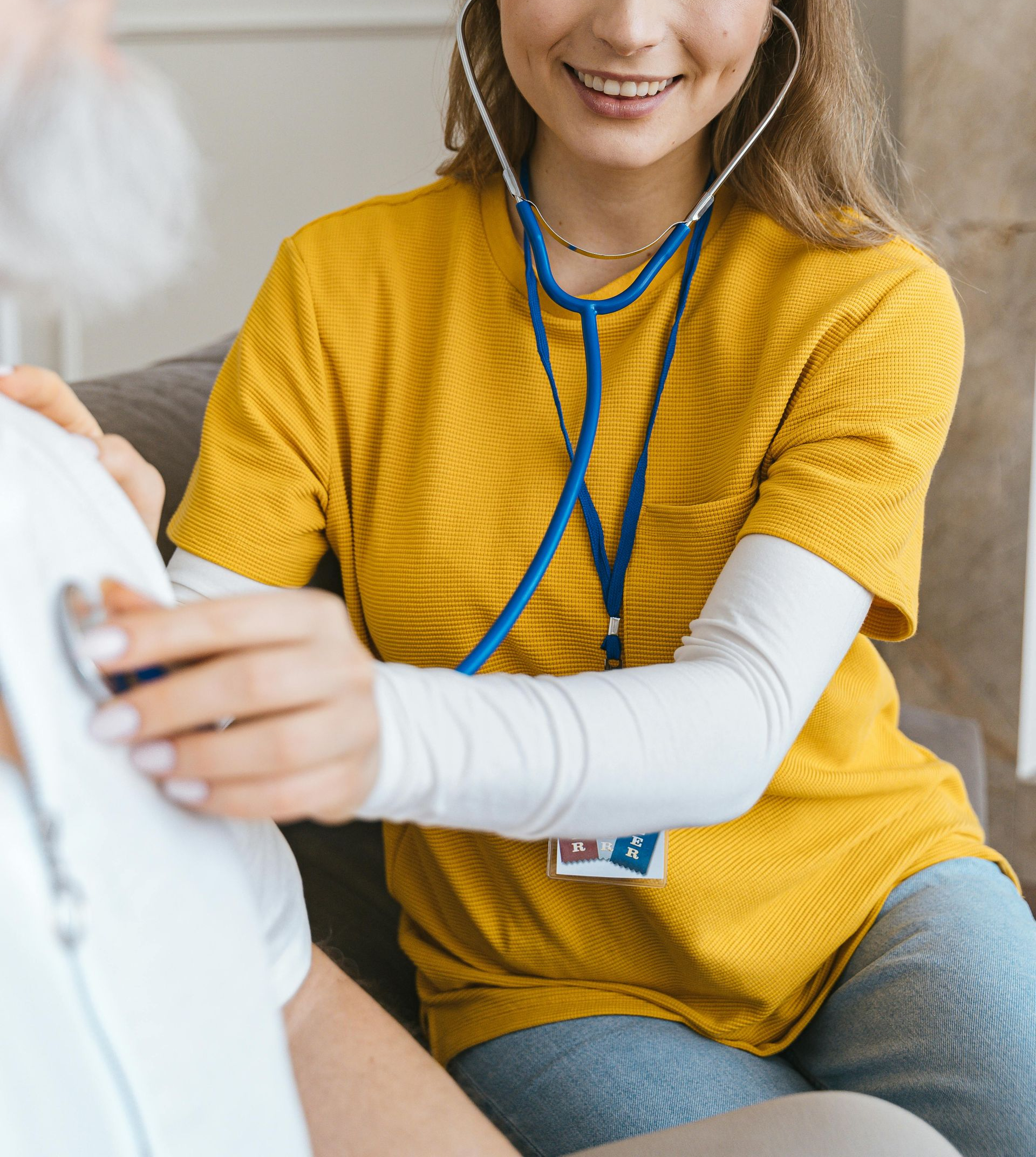 Health worker in yellow shirt using a stethoscope to examine a patient indoors