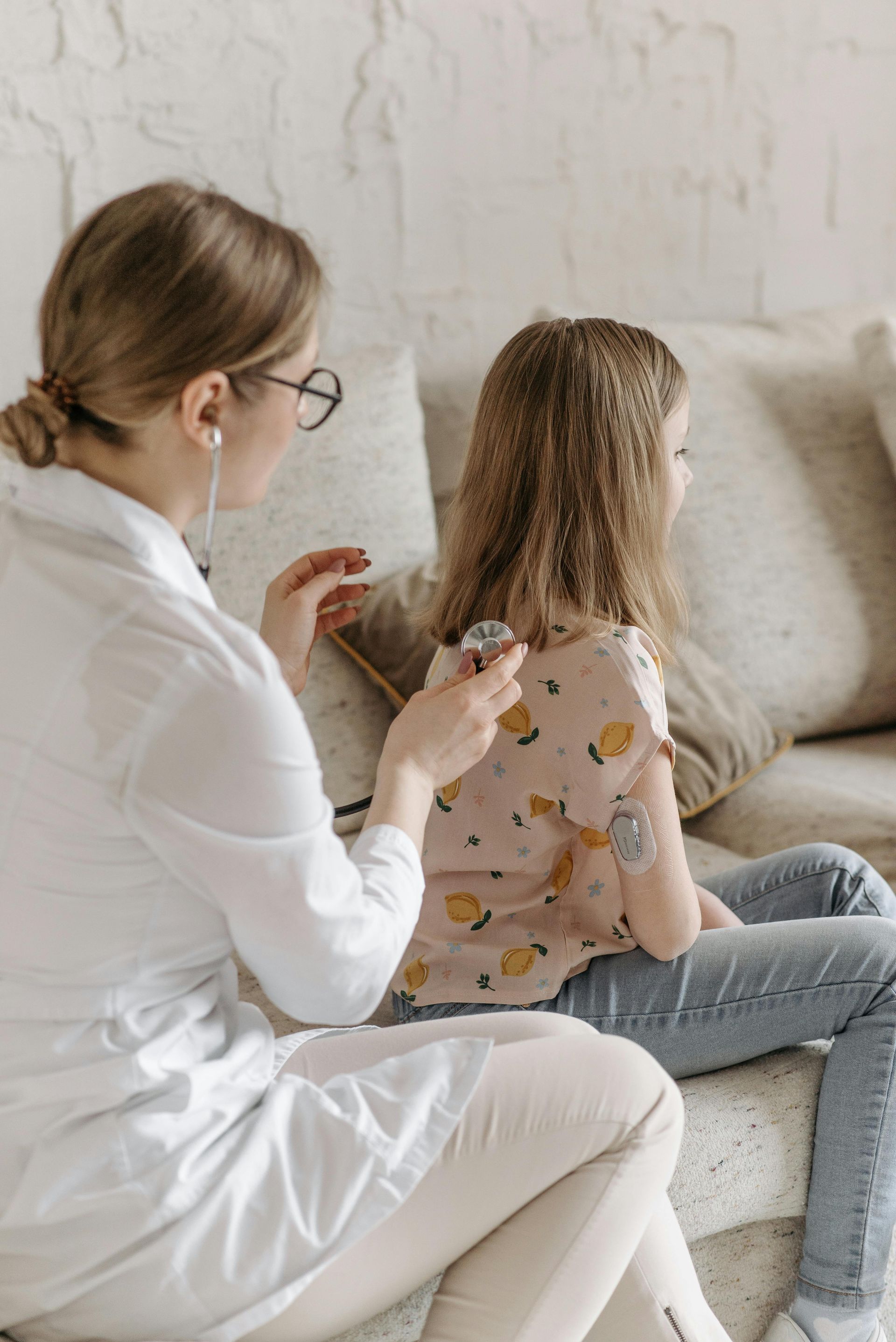 Doctor examining a child’s back while they sit together on a couch