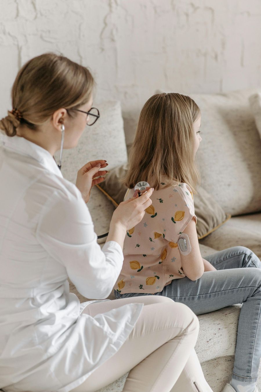 Medical professional examining a child sitting on a couch in a living room