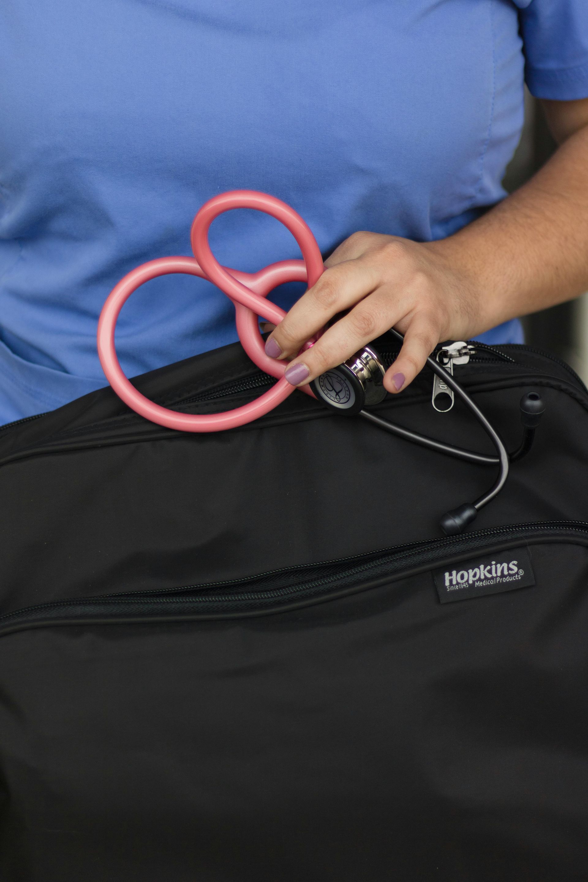 Person holding pink tubing and black device near a black bag, wearing a blue shirt.
