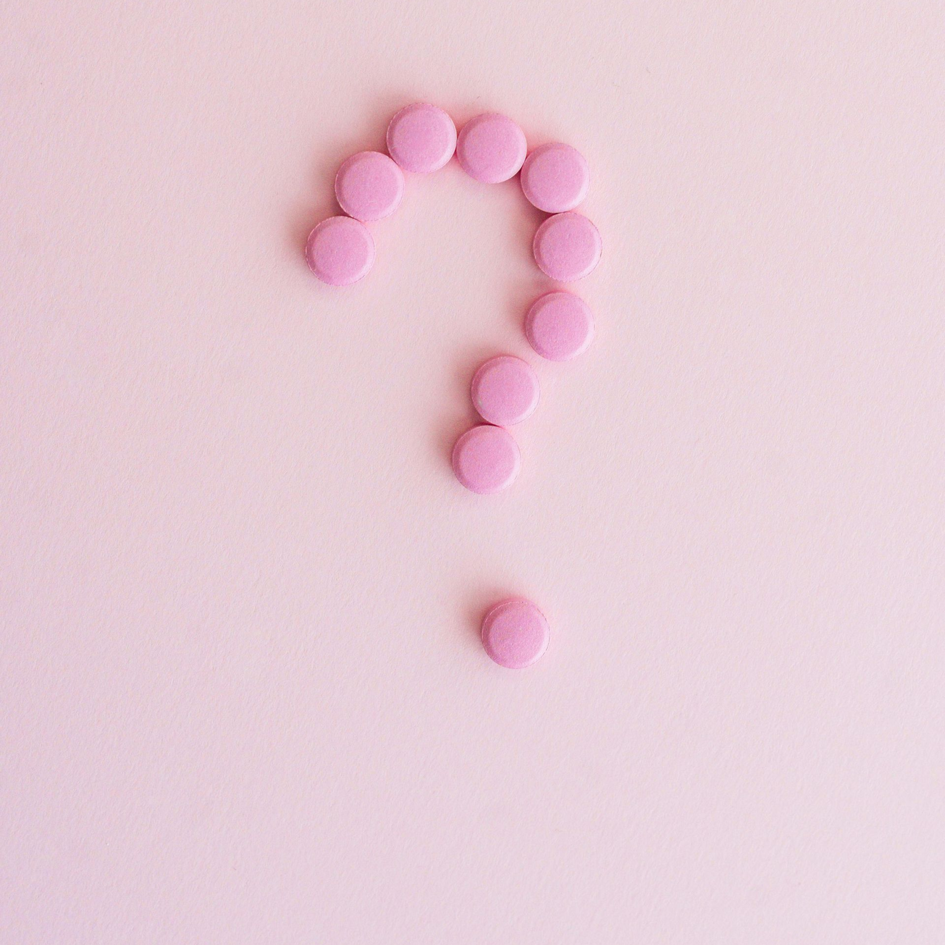 Pink beads arranged in a question mark on a pale pink background
