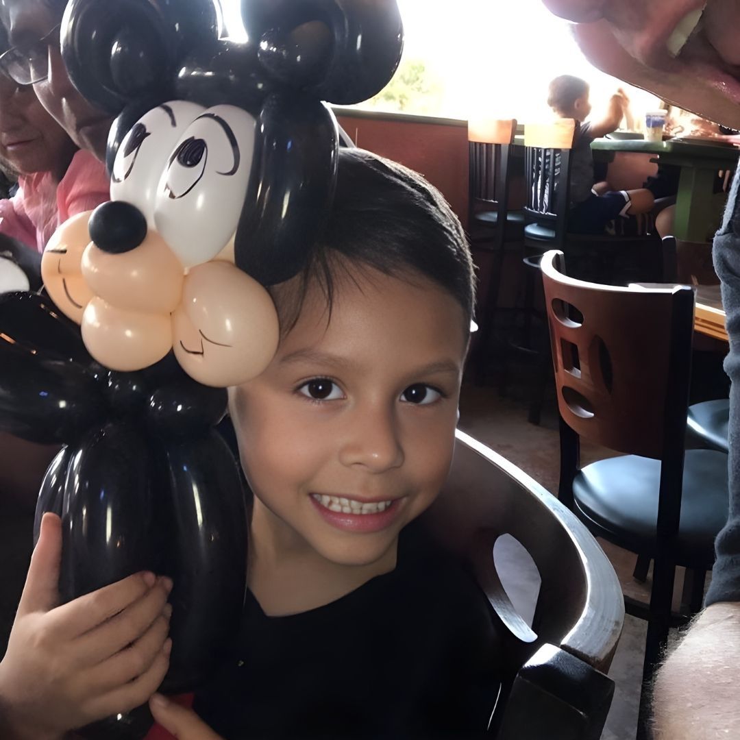 Smiling child wearing a Mickey Mouse balloon hat. Restaurant setting.
