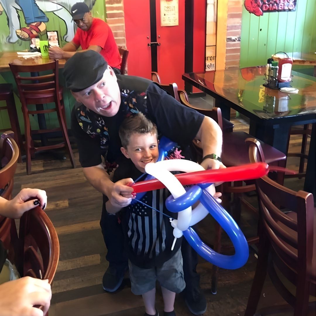 Man and boy holding balloon airplane in a restaurant, man smiling.