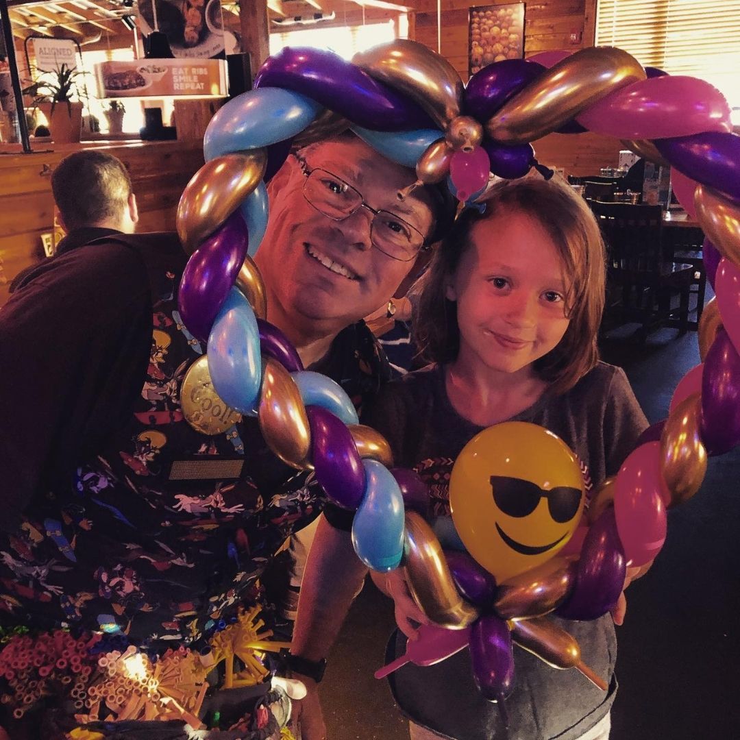 Man and child smiling, framed by a heart-shaped balloon arrangement with a smiley face balloon.