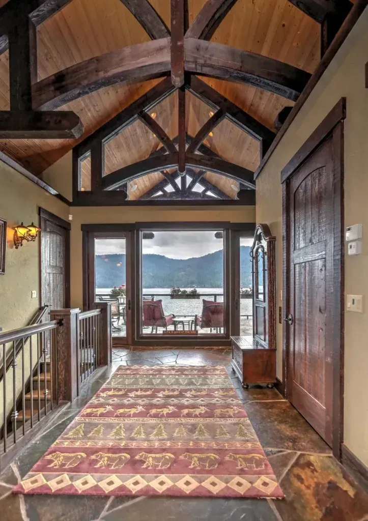 Hallway with high wood ceilings, large windows overlooking water, rug, and wooden door.