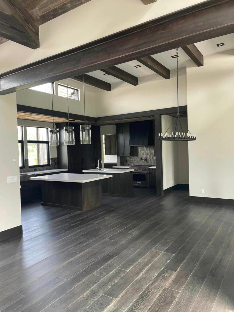 Open-concept kitchen and living area with dark wood floors, cabinets, and ceiling beams.
