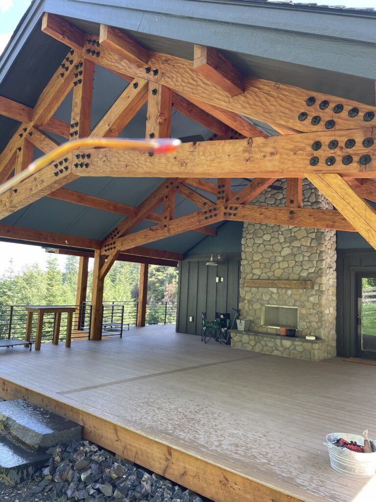 Covered patio with exposed wooden beams, stone fireplace, and gray roof.